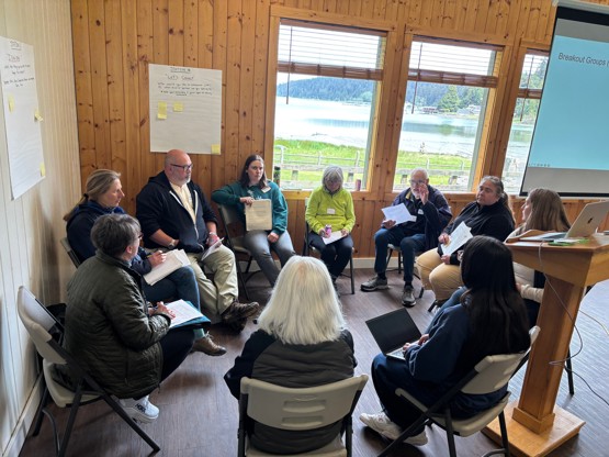 A group sits in a circle discussing forage fish research needs. 